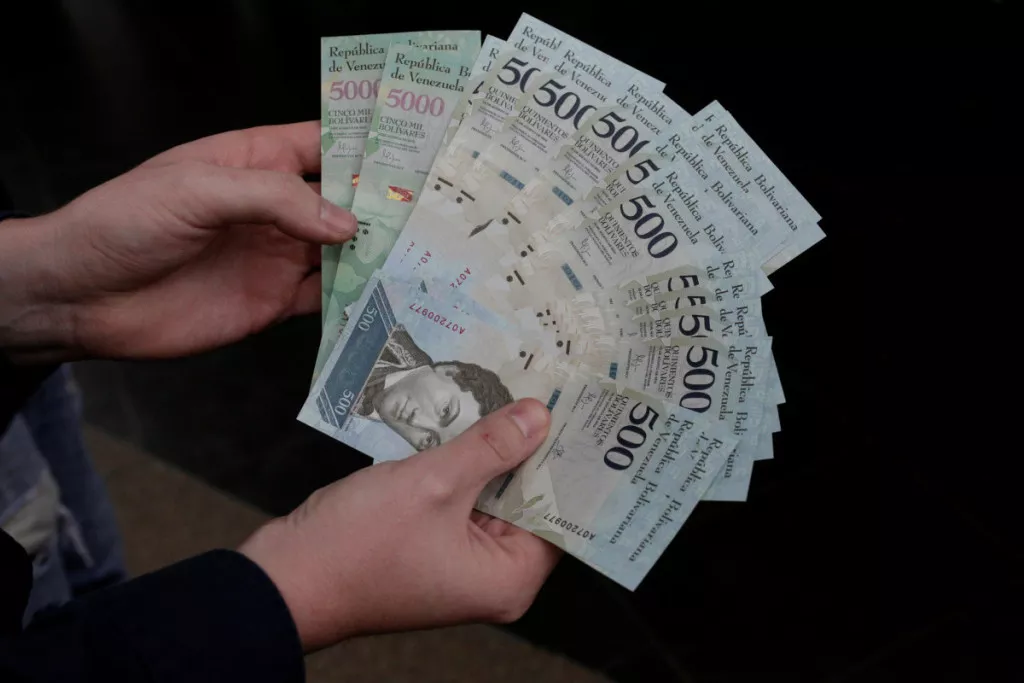 A man holds 500 and 5000 bolivar banknotes for a photo in Caracas